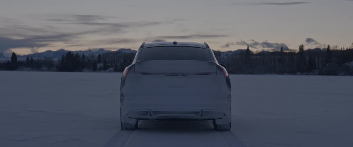 A vehicle parked on a snowy field with a mountain range trees the sky and clouds in the background