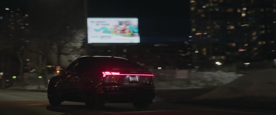 Car drives down city street past parking lots a digital billboard and a clinic at night