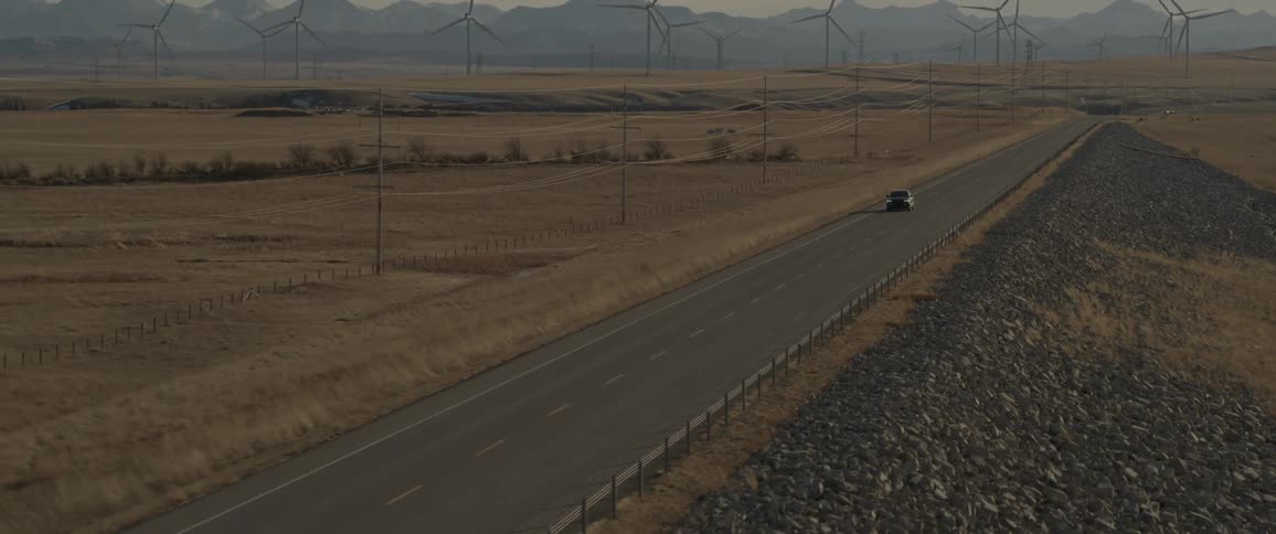 A black audi car is driving on a freeway with windmills visible in the background