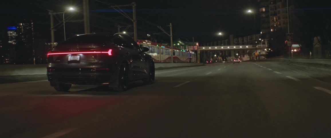 A vehicle driving on a city road with a train buildings and streetlights in the background