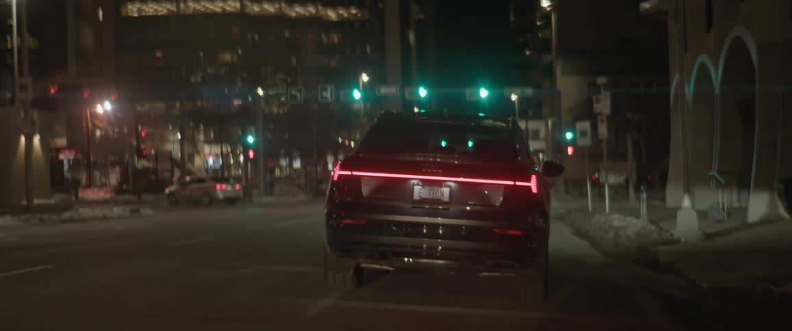 A black audi car is driving on a city road with buildings in sight