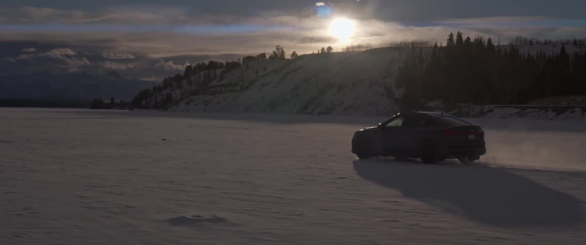 A black car dives through the snow as the sun is setting