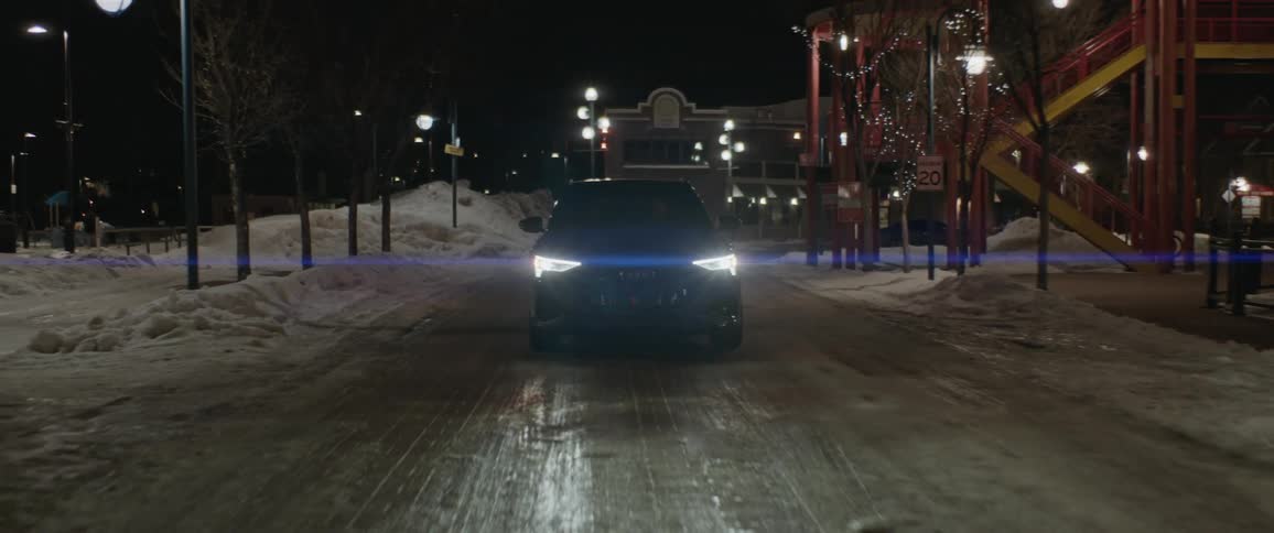 Black car with headlights on driving on a road in a town at night