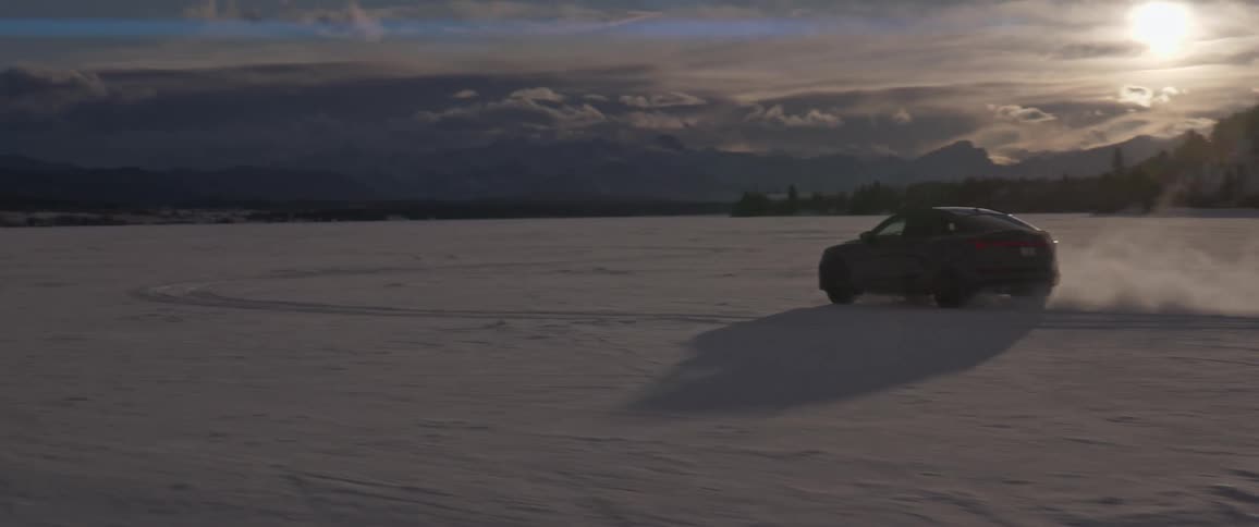 A black automobile travels through the snow as the sun sets