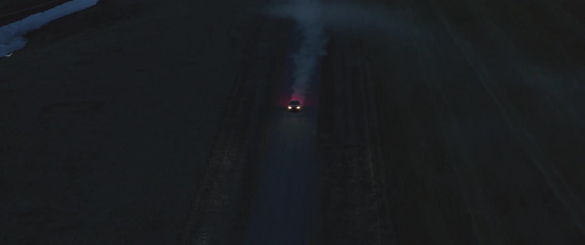 A car is driving down a road in a rural area at night