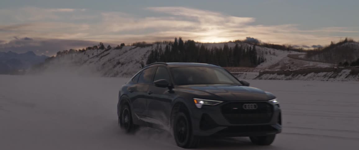 Audi car drives in the snowy field with hills in the background at dusk