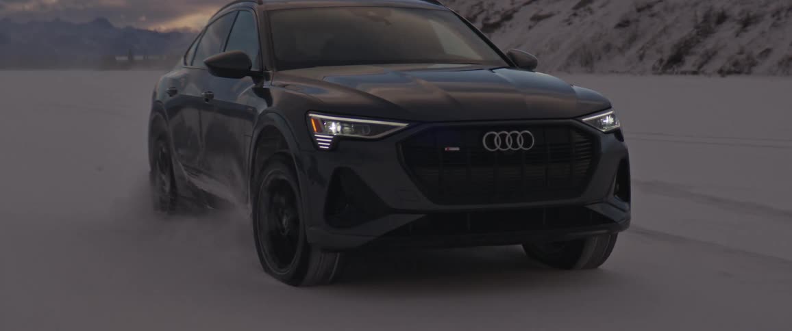 Black sports car parked on the white plains of a desert near the mountains at sunset