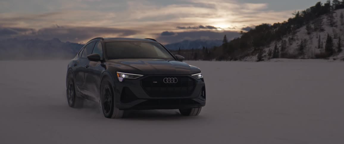 Dark grey audi car drives on snowy field at sunset