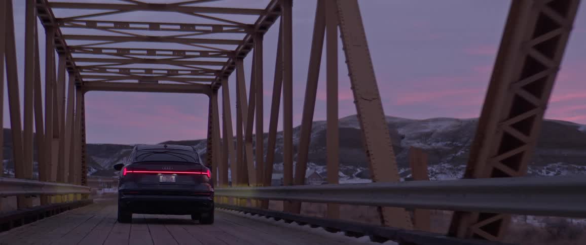 Black sports car driving over a bridge in the countryside near the mountains at morning