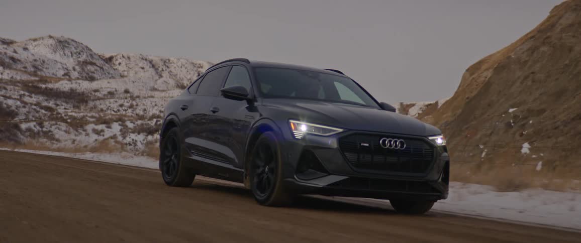 A black car travels on a road with snow covered mountains in the distance