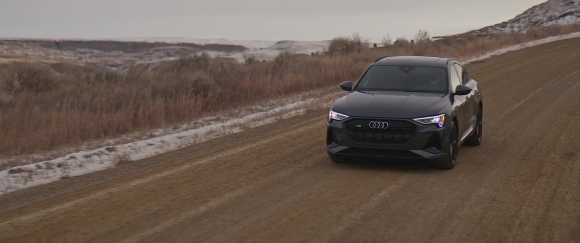 A vehicle driving on a dirt road with a landscape the sky and clouds in the background