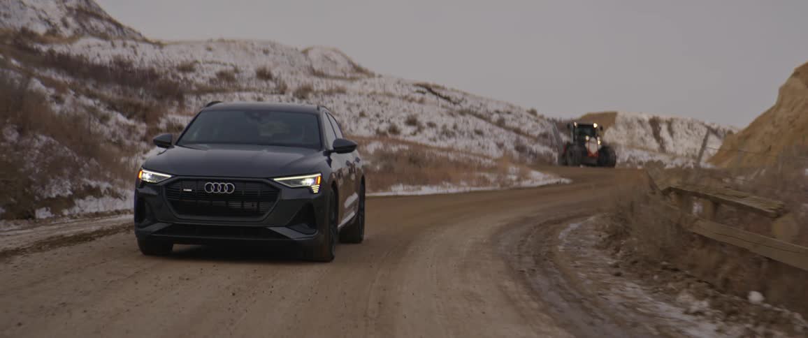 A black car travels on a road with snow covered mountains in the distance