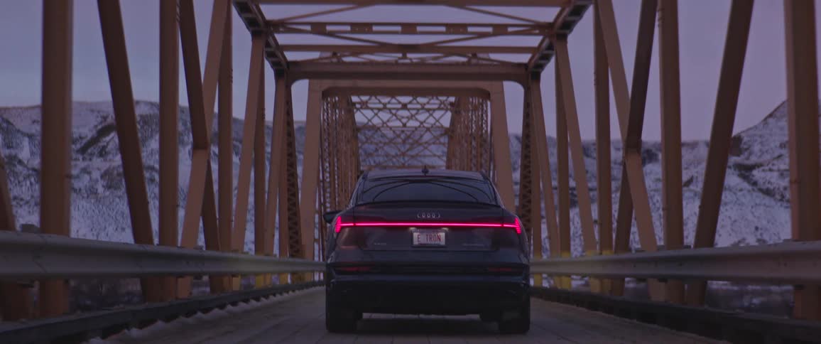 A vehicle driving on a bridge with a mountain range the sky and clouds in the background