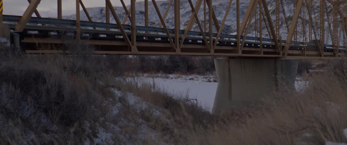 Black sports car driving over a bridge in the countryside near the mountains at morning