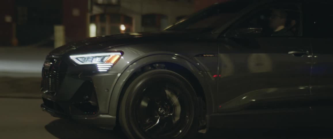 A dark sedan is driving down a dark city street