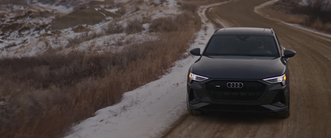 A black audi car is driving on a road during snowy season