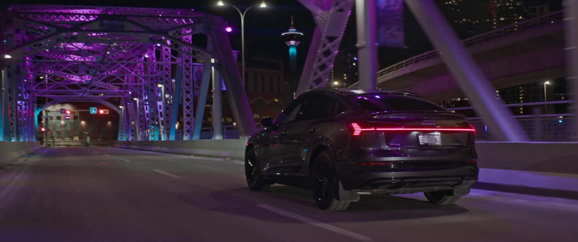 Black car driving over a bridge with colorful lights into the city at night