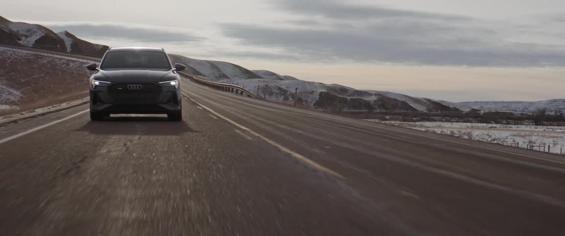 A vehicle drives along a rural road with snowy mountains in the distance