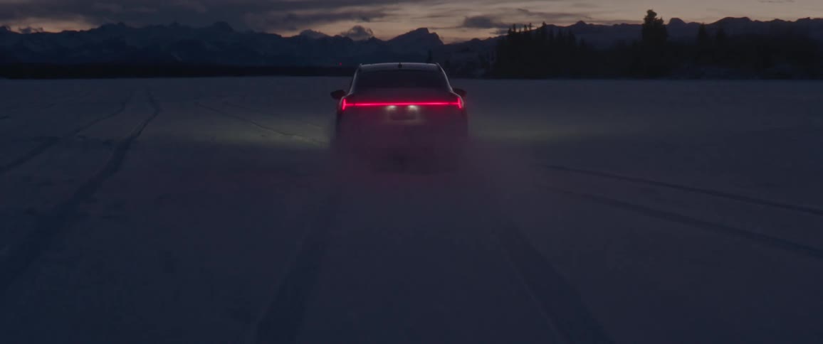 A vehicle driving on a snowy field with a mountain range trees the sky and clouds in the background
