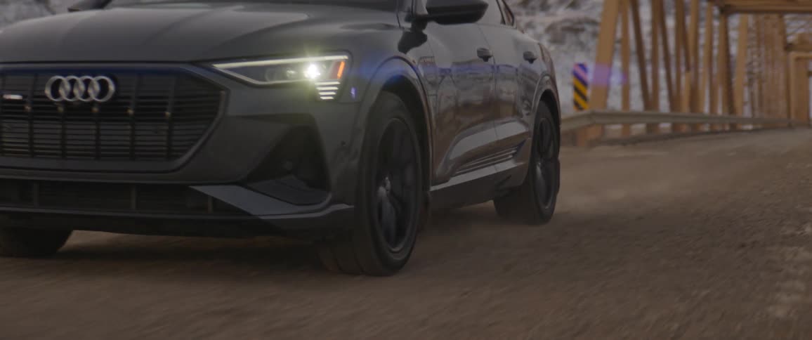 An audi car drives over a bridge away from snow covered mountains
