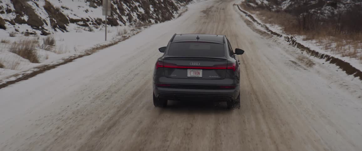 A vehicle driving on a snowy road with the sky and clouds in the background