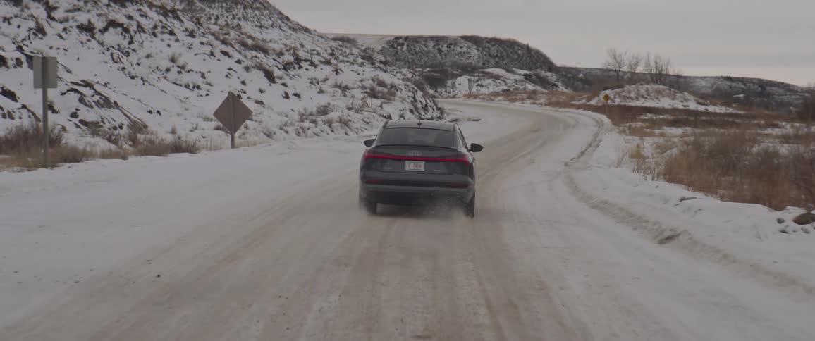 Black car driving on a snow covered road in the countryside at morning