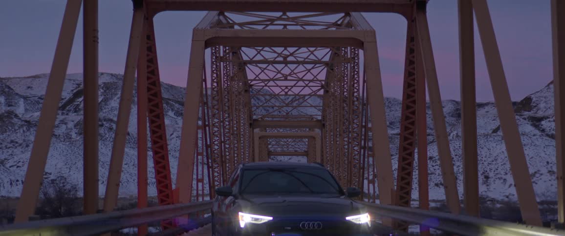 A car is parked on a bridge near the mountains at dusk