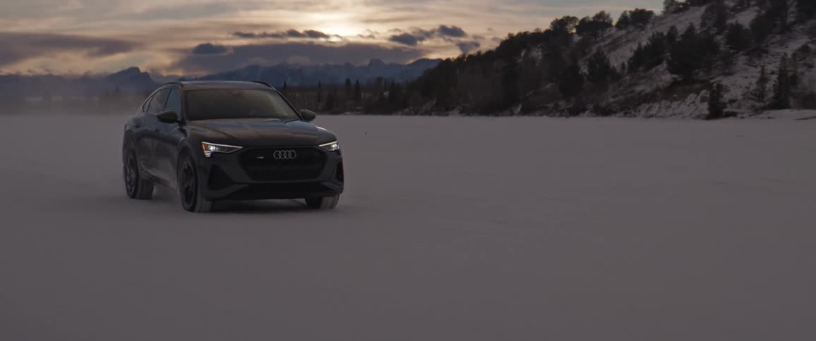 A vehicle drives a large open area next to snow dusted mountains