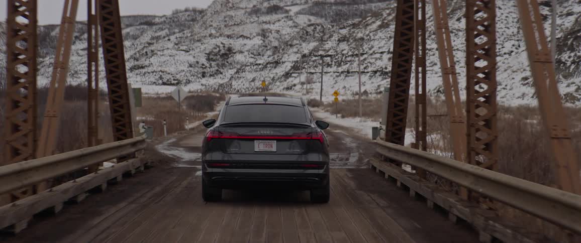 A vehicle driving on a bridge with a mountain range the sky and clouds in the background