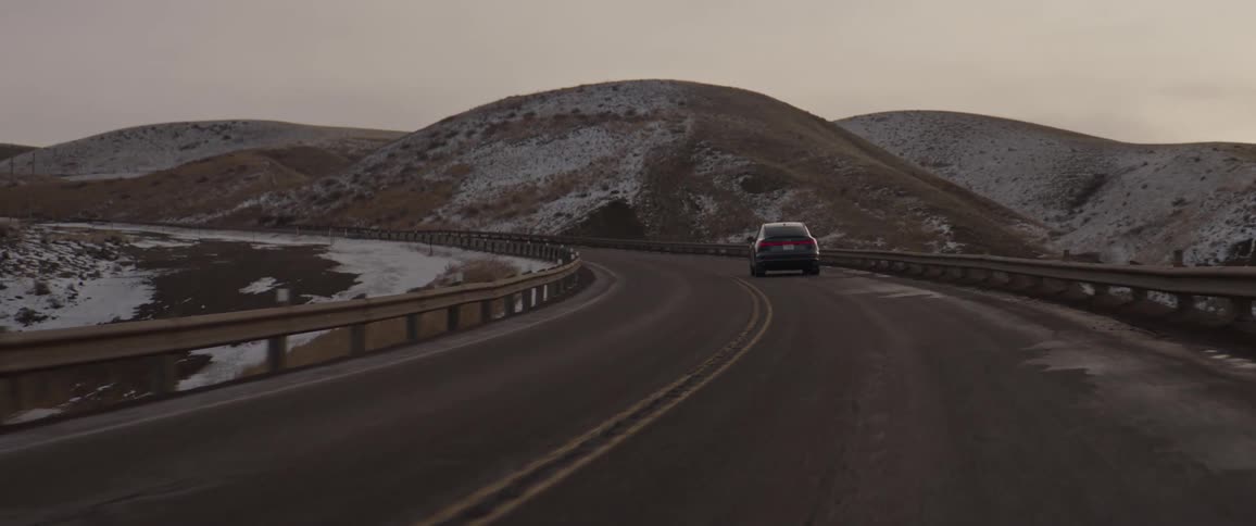 A vehicle driving on a road with hills the sky and clouds in the background