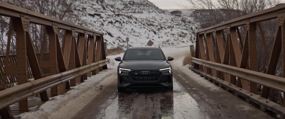 A vehicle driving on a bridge with a mountain range the sky and clouds in the background