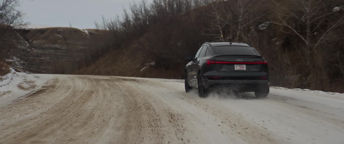 A vehicle travels through a hill countryside along a road covered in muddy snow during the day