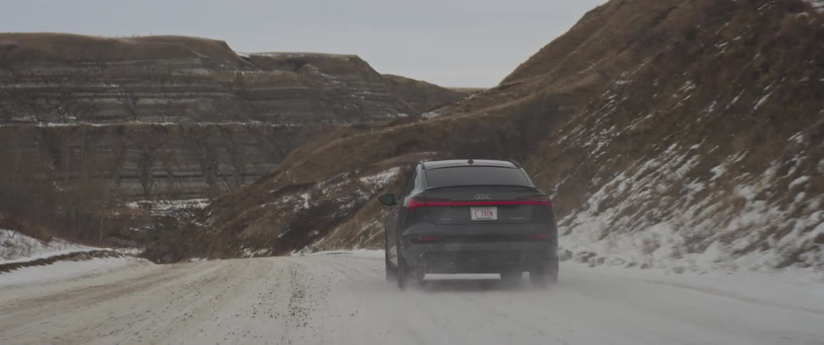 Dark grey audi car drives downhill on snowy road