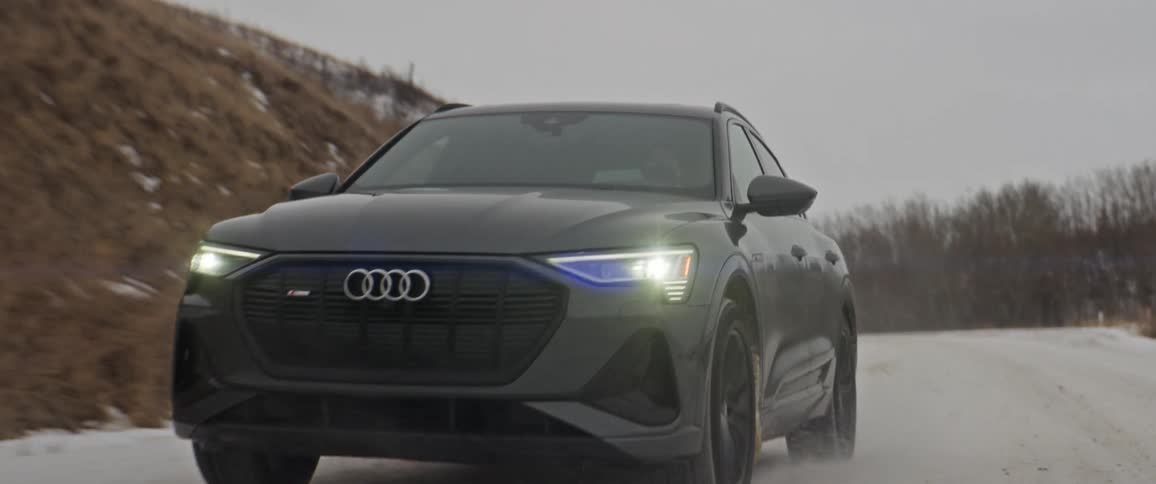 Black car with headlights on driving on a countryside road covered in snow