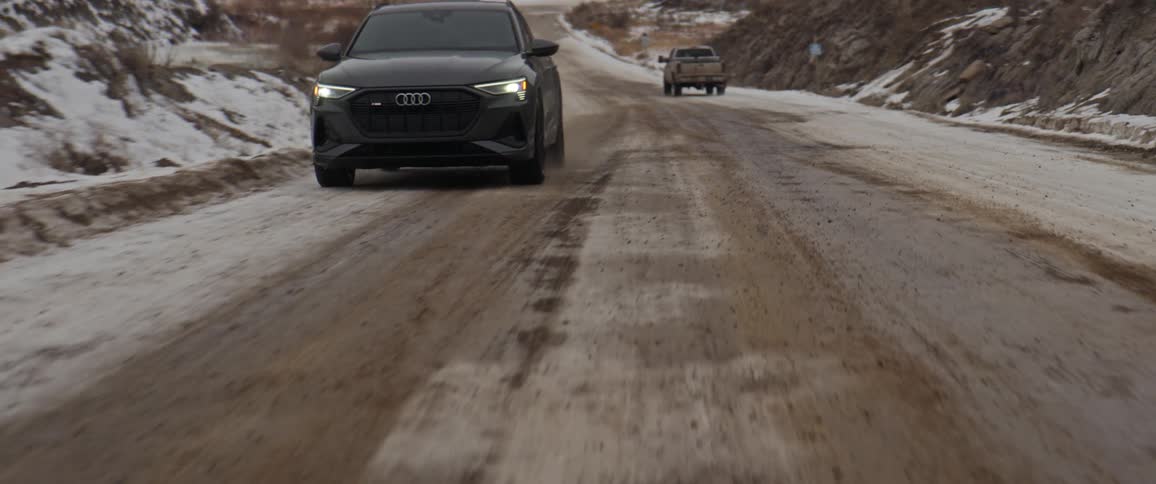 A car and truck are driving on a road in winter