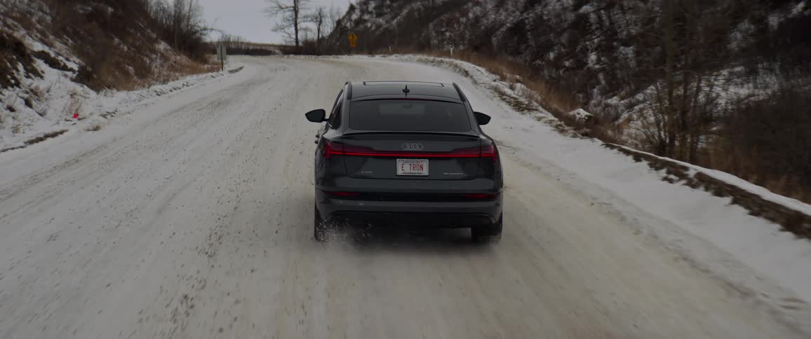 A vehicle driving on a snowy road with trees the sky and clouds in the background