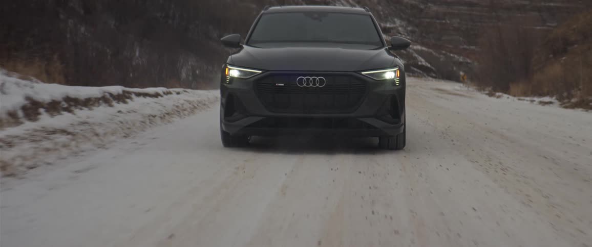 Black car driving on a snow covered road near the mountains at morning