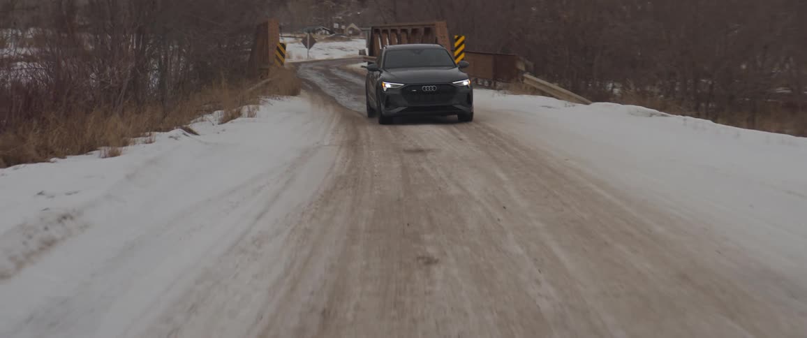 A vehicle drives a snow covered road and small rural bridge