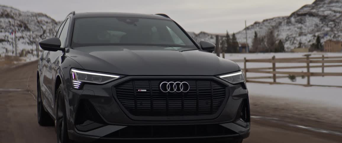 A black audi car is driving on a road during snowy season