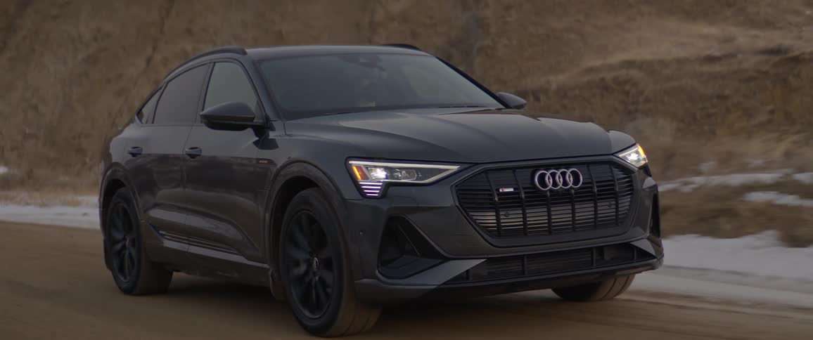 A black audi automobile travels on a road with a mountain pass in the distance