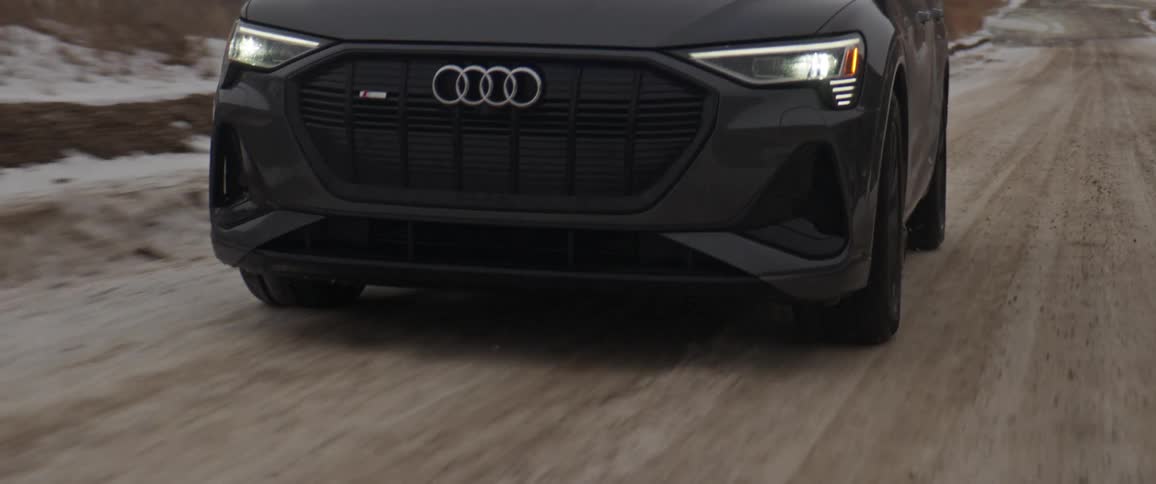 Dark grey audi car drives uphill on dirt road with snowy hills in the background