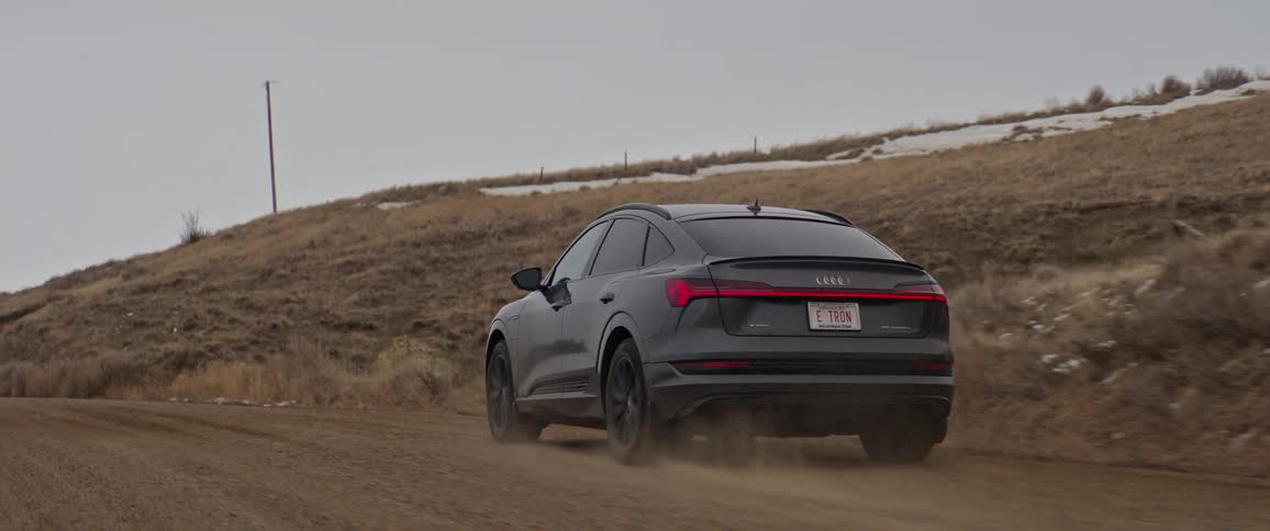 A vehicle driving on a dirt road with a hill the sky and clouds in the background