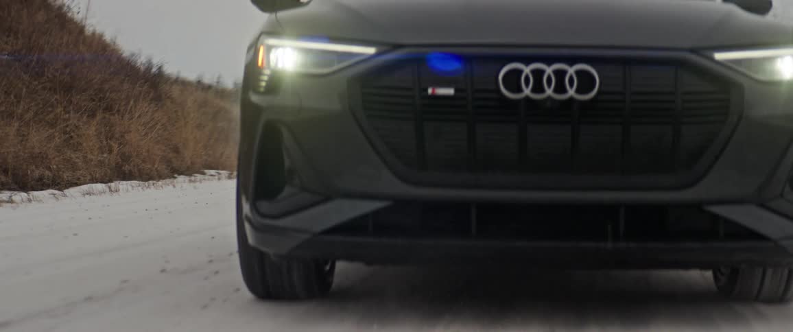 Dark grey audi car drives on snowy country road