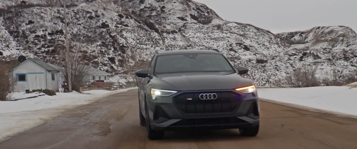 Dark audi car drives on highway with snowy mountains in the background