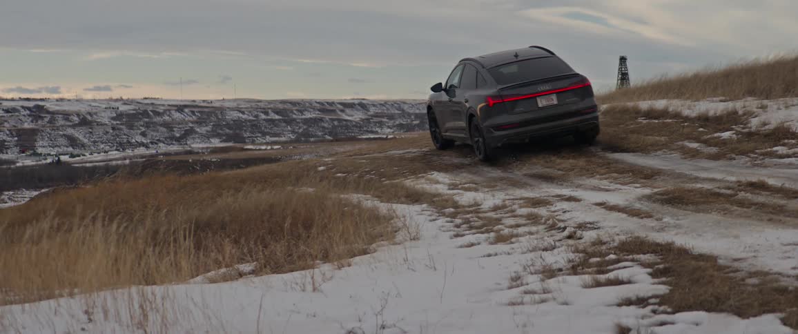 A vehicle driving on a grassy field with snow with the sky and clouds in the background