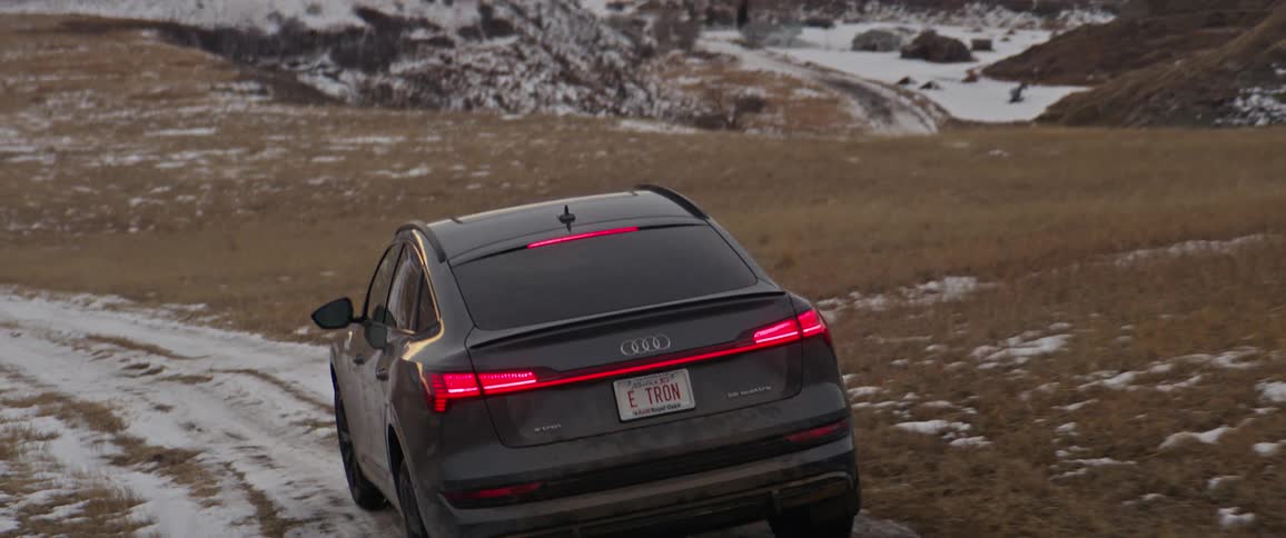 A vehicle driving on a dirt road covered in snow with the sky and clouds in the background