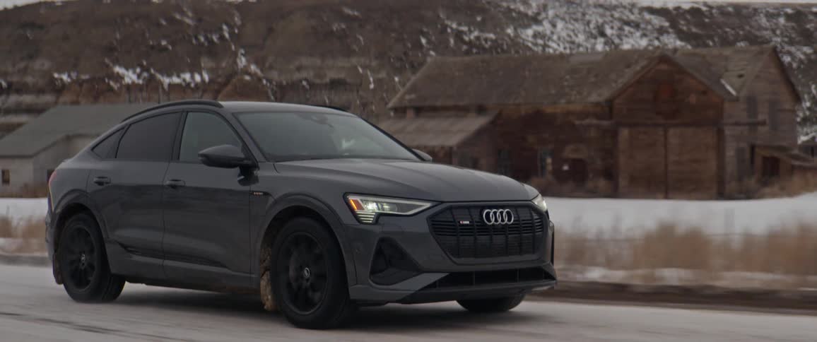 An audi vehicle drives a snow topped rural road beside a few cabins