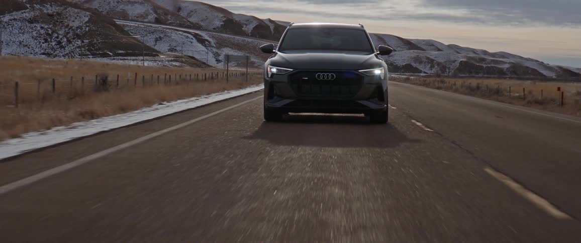 A black car travels on a road with snow covered mountains in the distance