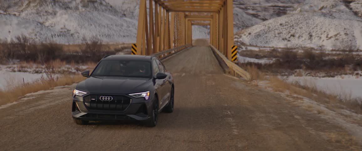 Black sports car driving over a bridge in the countryside near the mountains at morning