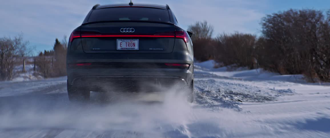 A black car travels on a snow covered road with trees along the roadside